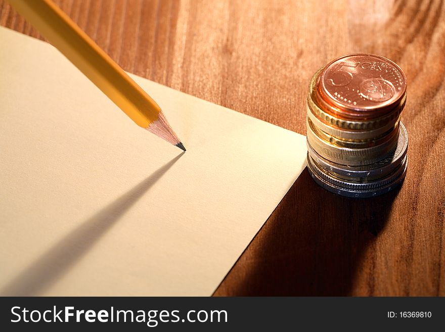 Column of coins near paper and pencil on wooden background. Column of coins near paper and pencil on wooden background