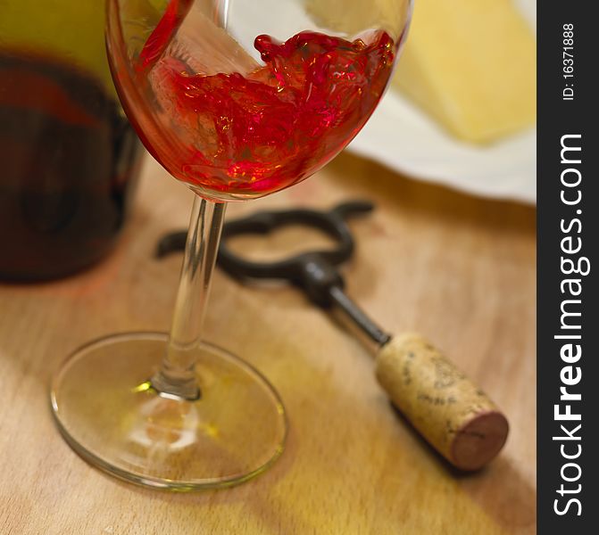 Close up of red rose wine poured into glass next to plate of cheese and corkscrew