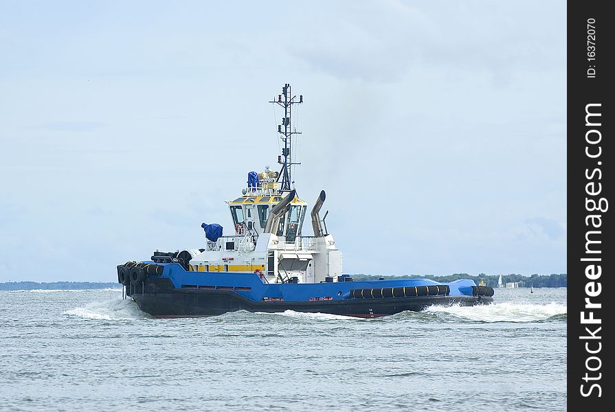 Large blue, white and yellow tugboat motoring for a ship. Large blue, white and yellow tugboat motoring for a ship