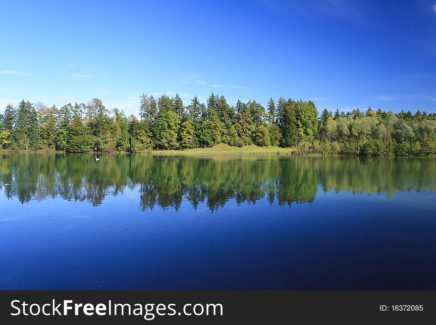 Blue lake with colorful wood and blue sky in autumn. Blue lake with colorful wood and blue sky in autumn