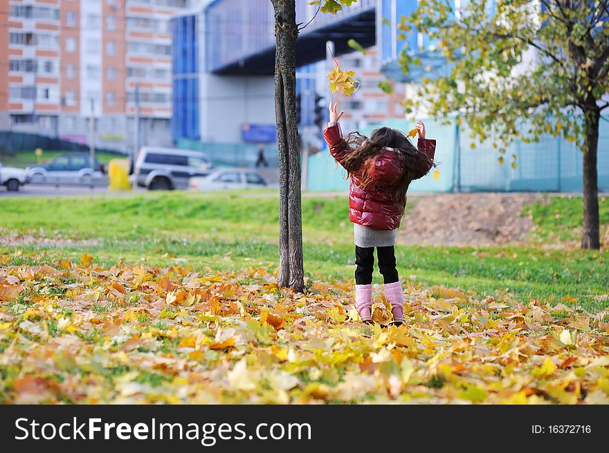 Adorablesmall girl with long dark hair in colorful clothers has fun in sunny autumn day in the park with yellow leaves. Adorablesmall girl with long dark hair in colorful clothers has fun in sunny autumn day in the park with yellow leaves