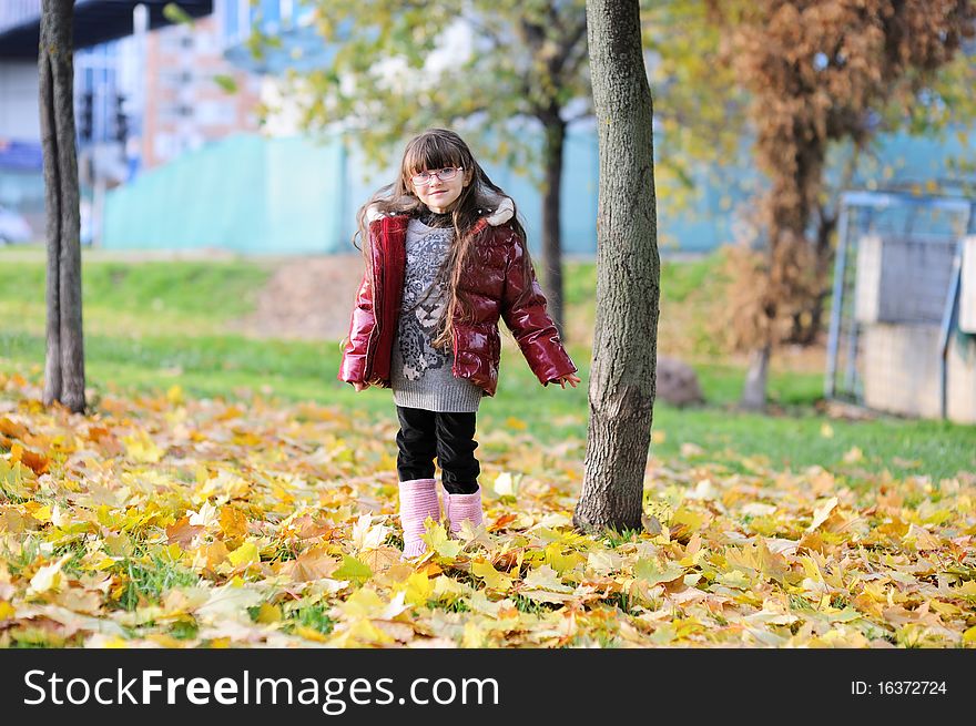 Adorablesmall girl with long dark hair in colorful clothers has fun in sunny autumn day in the park with yellow leaves. Adorablesmall girl with long dark hair in colorful clothers has fun in sunny autumn day in the park with yellow leaves