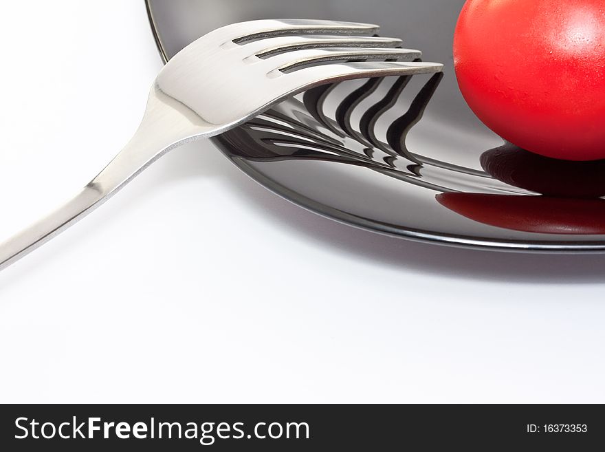 Red tomato on a black high-gloss plate with stainless fork. Red tomato on a black high-gloss plate with stainless fork