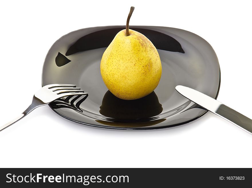 Fresh yellow pear on a black plate with fork and knife
