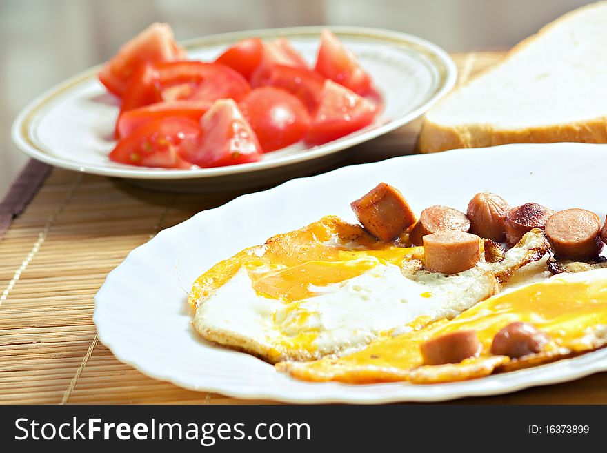 Breakfast with eggs, sausage, bread and tomato