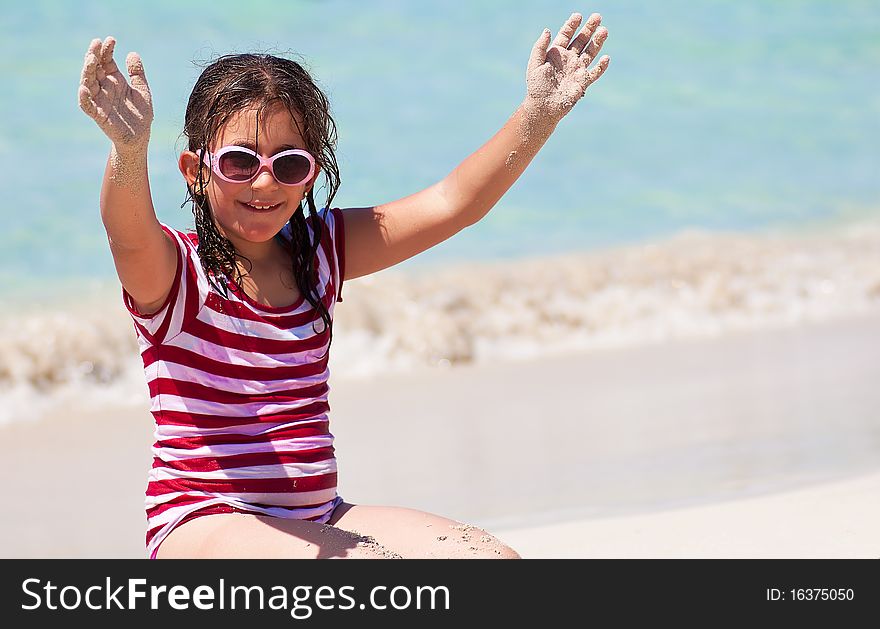 Beautiful girl with sunglasses sitting in the sand on a beach and raising her hands