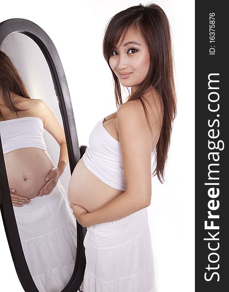 A woman in white with her belly showing is standing by a mirror. A woman in white with her belly showing is standing by a mirror.