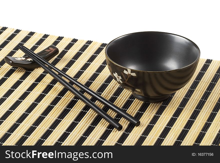 Wooden chopsticks and little ceramic bowl on the bamboo mat over white background. Wooden chopsticks and little ceramic bowl on the bamboo mat over white background