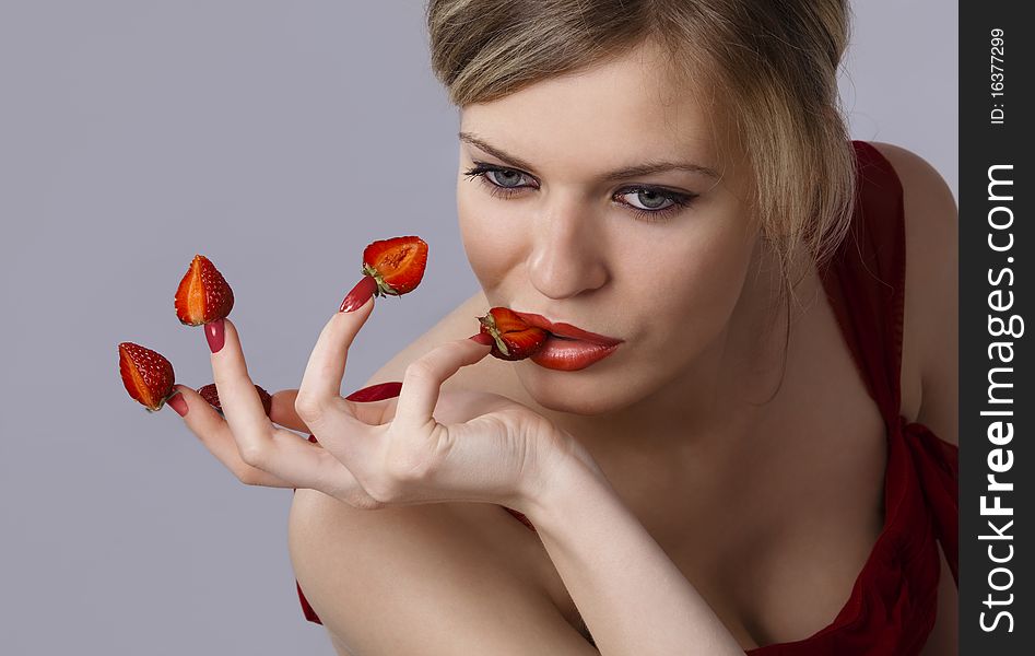 young woman with red strawberries picked on fingertips isolated on gray background