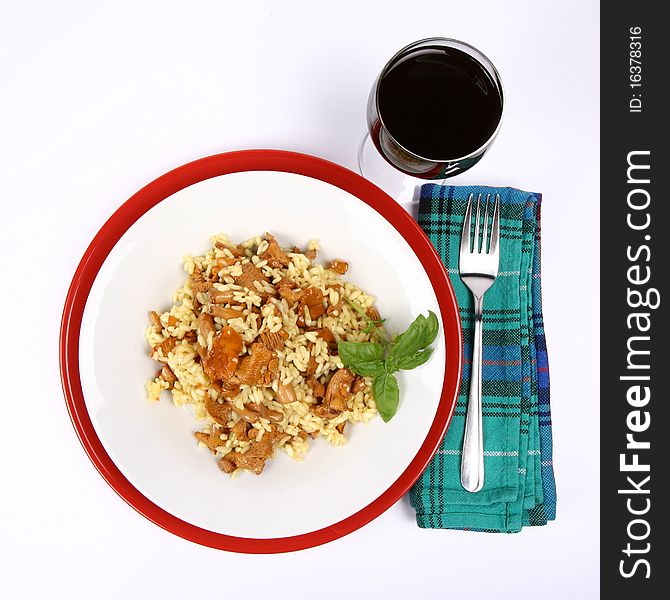 Risotto with mushrooms on a plate decorated with basil, glass of red wine and a fork on a napkin