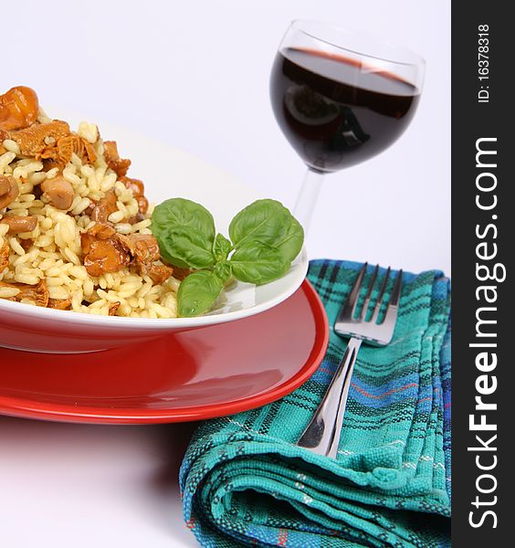 Risotto with mushrooms on a plate decorated with basil, glass of red wine and a fork on a napkin, in close up