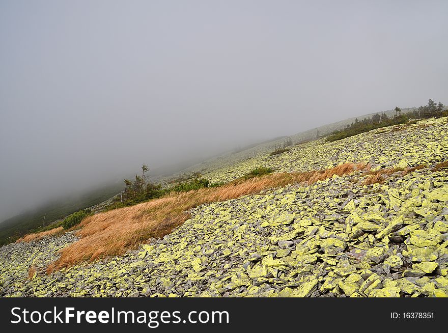 A mountain stone slope in a fog in a landscape with a yellow autumn grass. A mountain stone slope in a fog in a landscape with a yellow autumn grass.