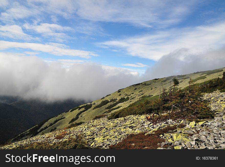 A mountain stone slope in a fog in a landscape with the dark blue sky. A mountain stone slope in a fog in a landscape with the dark blue sky