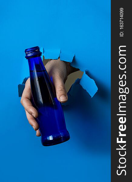 A hand holds a blue water bottle from a torn paper hole