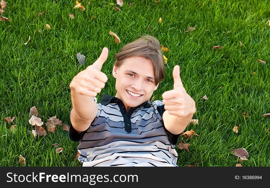 Young man lying on the grass with thumbs up. Young man lying on the grass with thumbs up