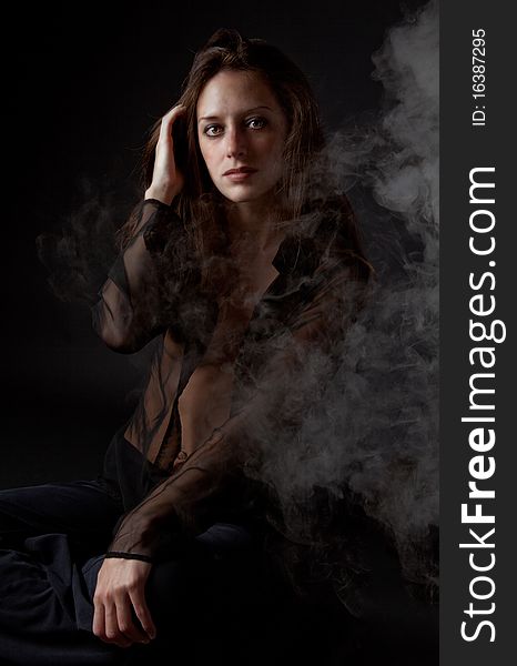A dramatic image of a gorgeous woman in a sheer black top against a black background with smoke floating around her. A dramatic image of a gorgeous woman in a sheer black top against a black background with smoke floating around her