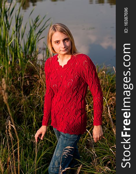 A girl in red pullover standing in in front of a pond