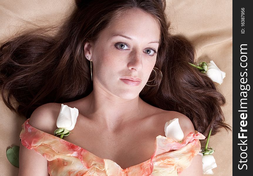 A beautiful portrait of a lovely woman lying on a bed, surrounded by white roses. A beautiful portrait of a lovely woman lying on a bed, surrounded by white roses