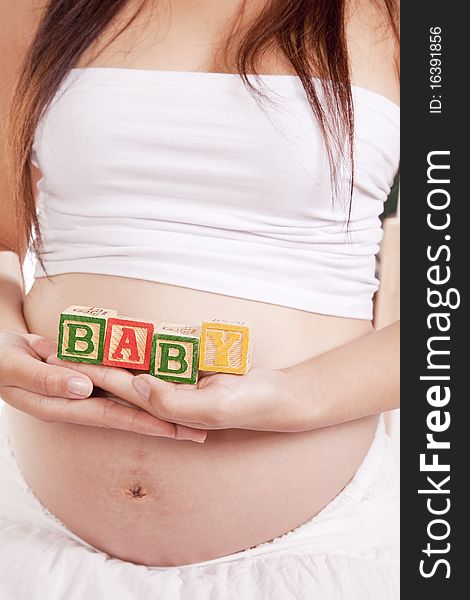 A pregnant woman holding blocks that spell baby. A pregnant woman holding blocks that spell baby