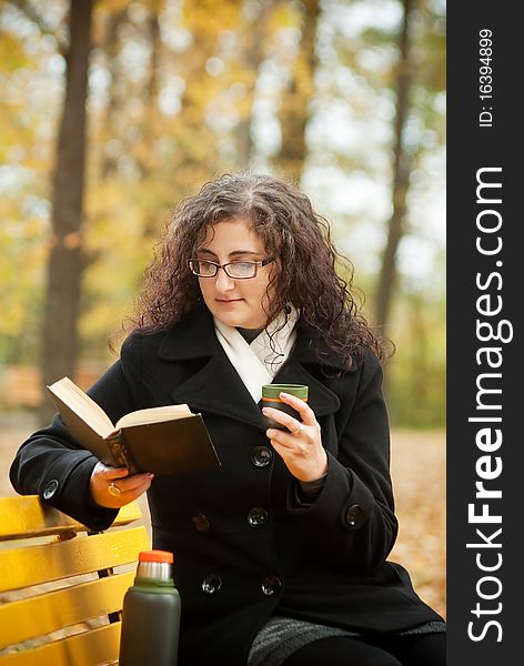 Young woman reading book and drinkin coffee on bench