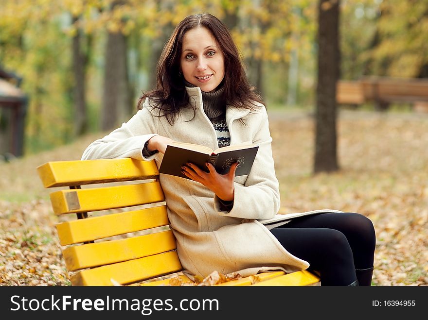 Young woman sitting on bench in autumn park with book
