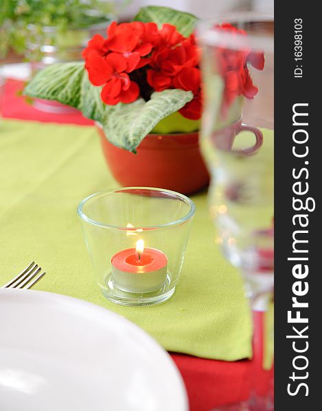 Red candle in a glass candlestick and flowers on the table in red and green colors