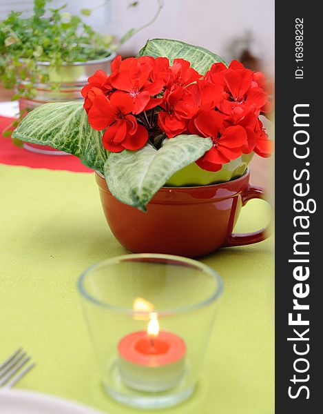 Red candle in a glass candlestick and flowers on the table in red and green colors