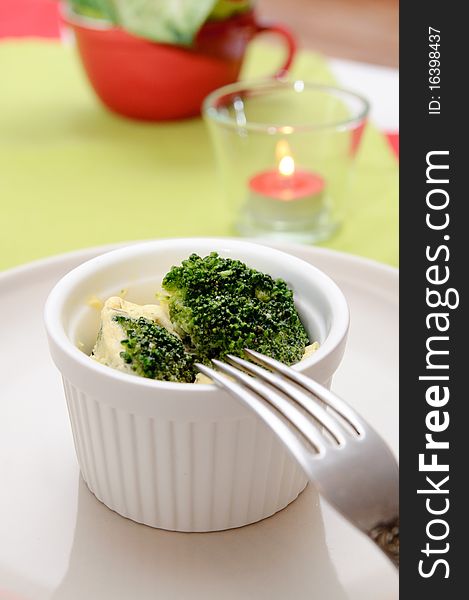 Omelet with broccoli in a white ceramic pot, and candles on the table in red and green colors