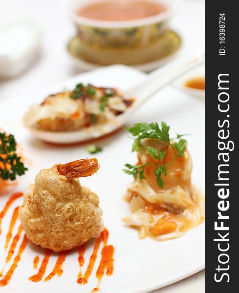 A plate of mixed Chinese delicacies, placed on a white plate and having also soup and sauces on the background.