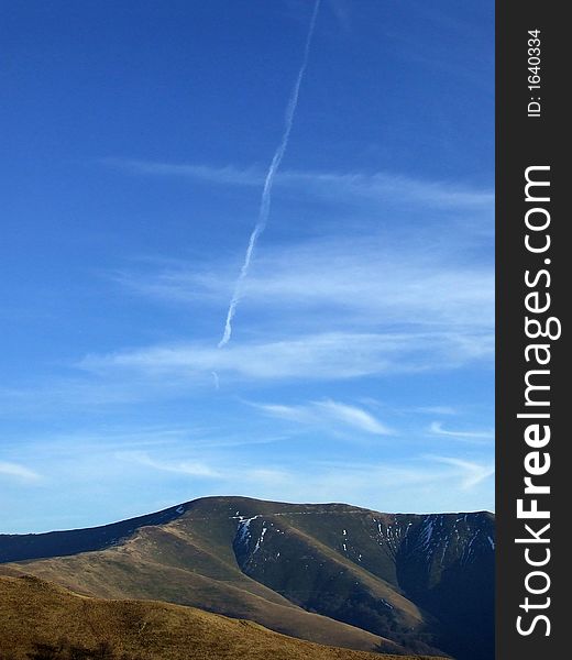 Scenic mountain landscape with airplane trail on the blue sky