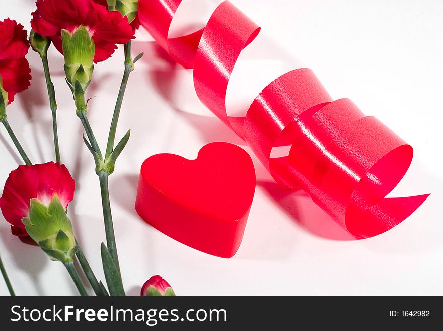Red plastic heart, twisted ribbon and red carnation on white background