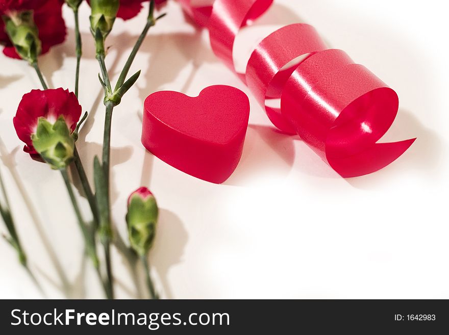 Red plastic heart, twisted ribbon and red carnation with white background. With copyspace