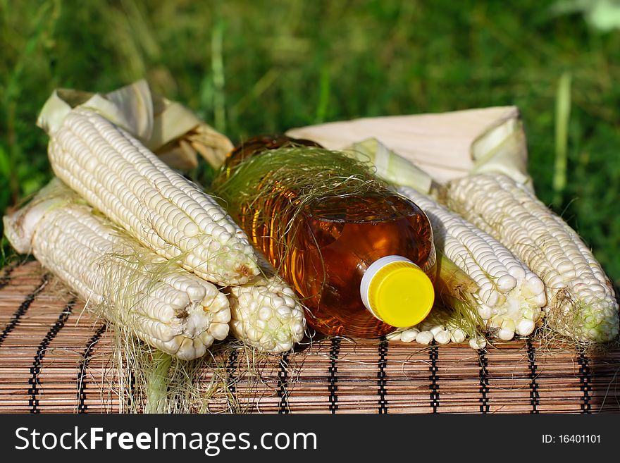 Freshlpicked corn on the cob and bottle of yellow oil. Freshlpicked corn on the cob and bottle of yellow oil.