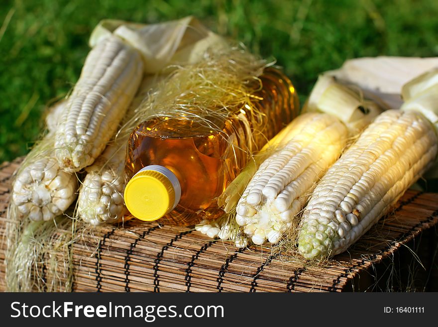 Freshlpicked corn on the cob and bottle of yellow oil. Freshlpicked corn on the cob and bottle of yellow oil.