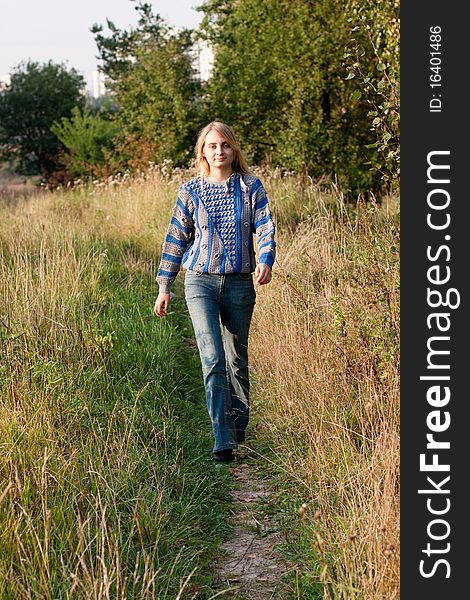 A girl in a blue and grey pullover and jeans walking along a woodside. A girl in a blue and grey pullover and jeans walking along a woodside