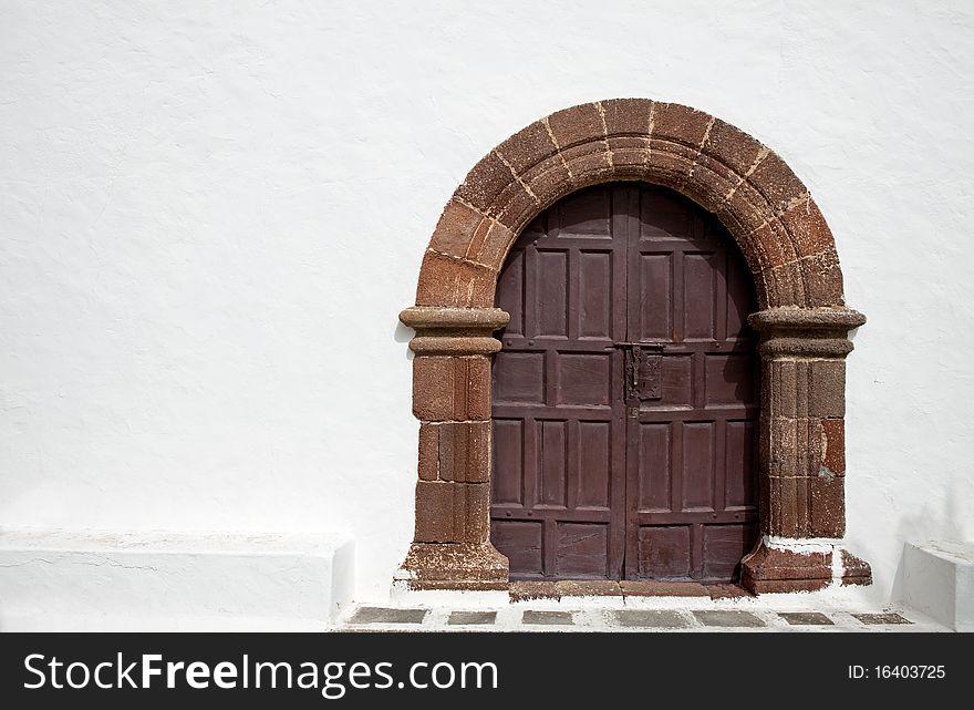Architectural detail - faded brown door in a whitewashed wall
