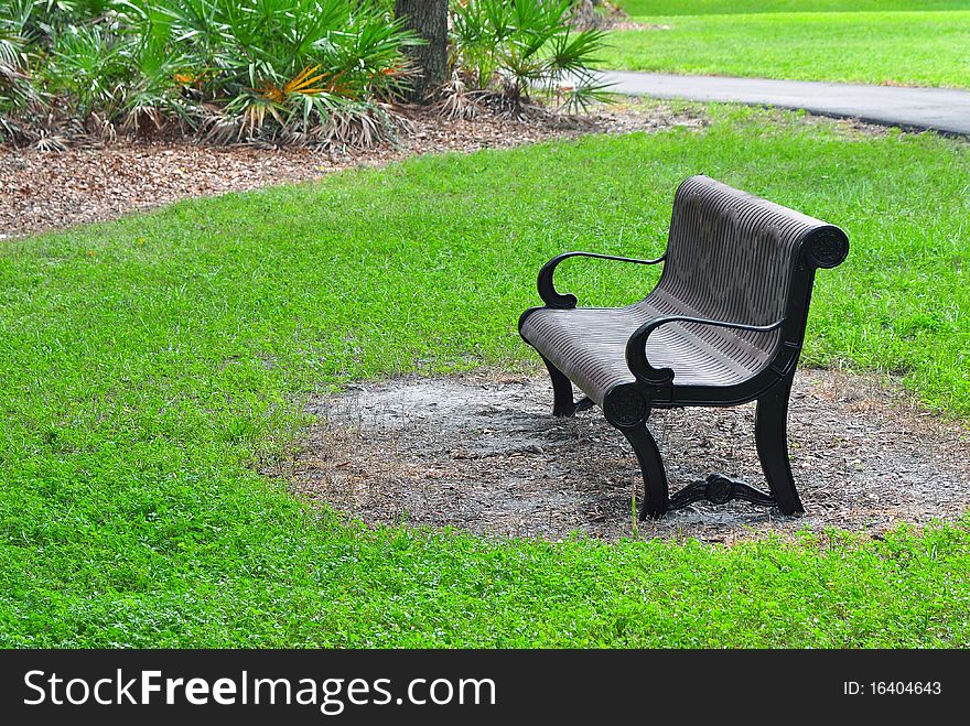 A metal bench painted in brown in a park surrounded by grass and trees. A metal bench painted in brown in a park surrounded by grass and trees.