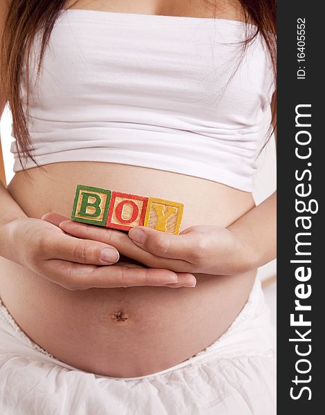 A pregnant woman holding blocks that spell boy. A pregnant woman holding blocks that spell boy
