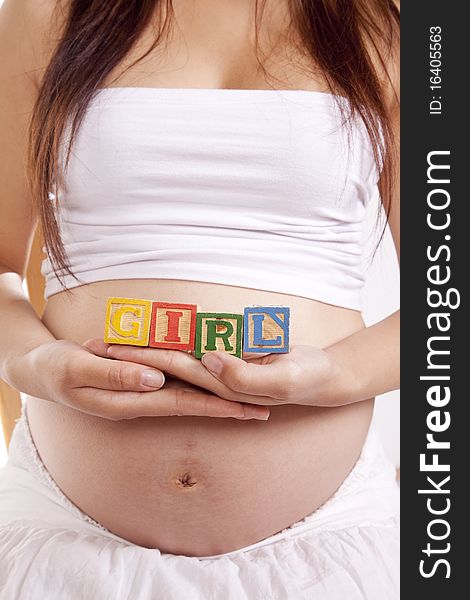 A pregnant woman is holding some blocks against her stomach that spell girl. A pregnant woman is holding some blocks against her stomach that spell girl