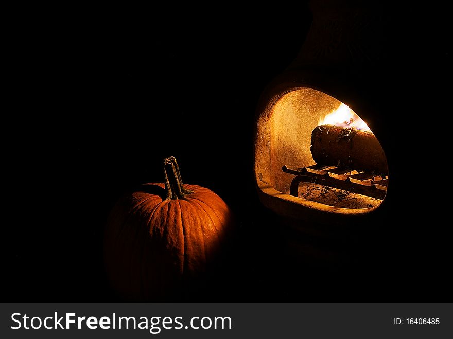 Pumpkin lit by firelight from a chiminea on black background. Pumpkin lit by firelight from a chiminea on black background