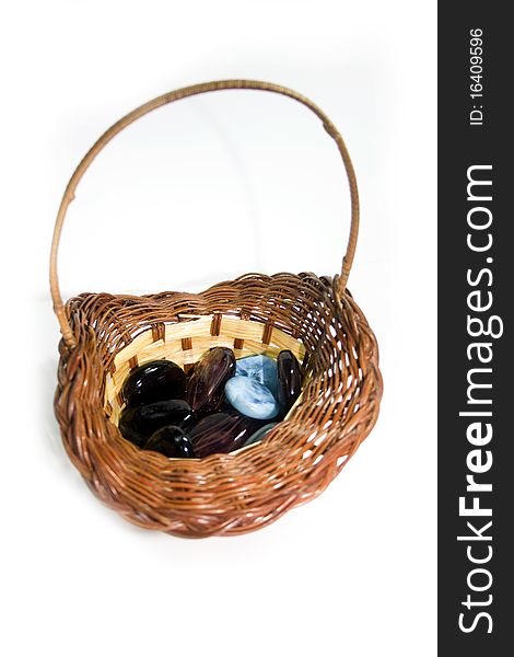 Some colored pieces of stone and glass in a straw basket, isolated on white. Some colored pieces of stone and glass in a straw basket, isolated on white