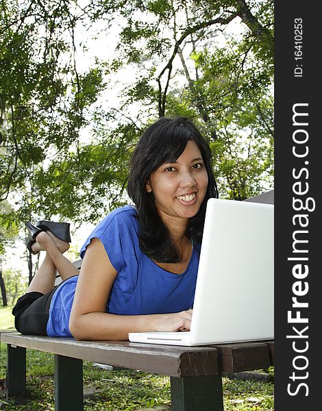 An Asian woman using her laptop on a park bench. An Asian woman using her laptop on a park bench