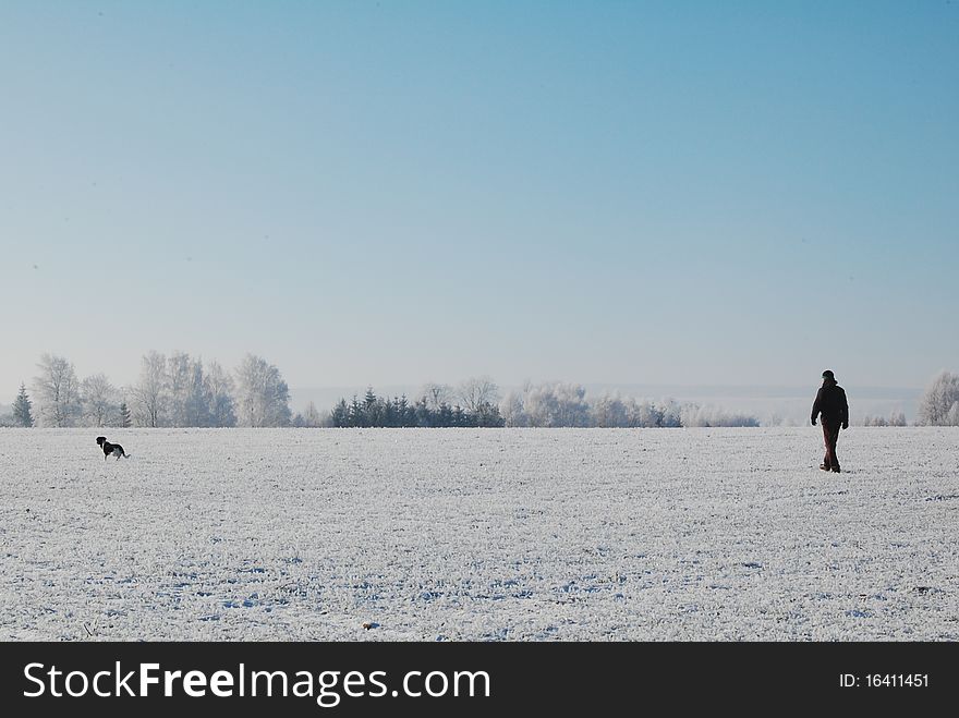 Silhouette of man and the dog in the snow-covered field.