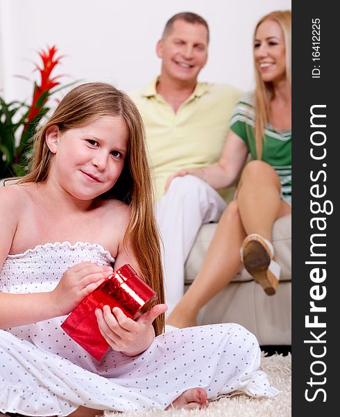 Cute girl unwrapping her christmas gift with parents in the background. Cute girl unwrapping her christmas gift with parents in the background