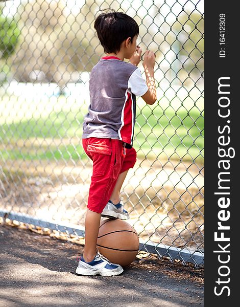 Rear view of young basketball player holding ball under his leg and and looking through fence