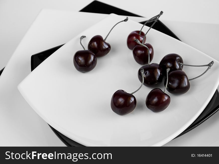 Nine black cherries on four black and white square dishes against the white background
