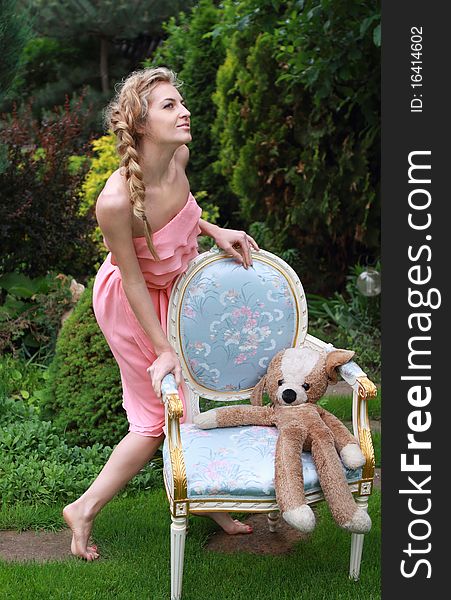 Attractive blond girl in the pink dress with toy in the garden. Attractive blond girl in the pink dress with toy in the garden