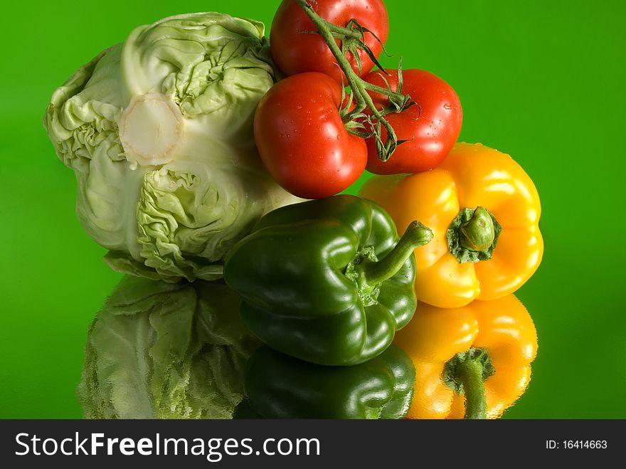 Vivid colorful still life with fresh vegetables: cabbage, tomatoes and paprika against the green background