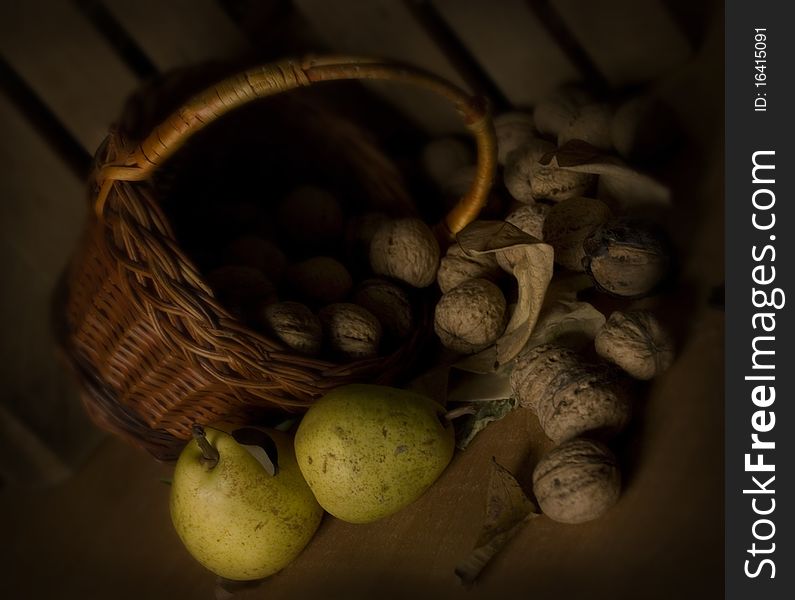 Green pears, nuts and basket against the dark wooden background, dark still life in vintage style. Green pears, nuts and basket against the dark wooden background, dark still life in vintage style