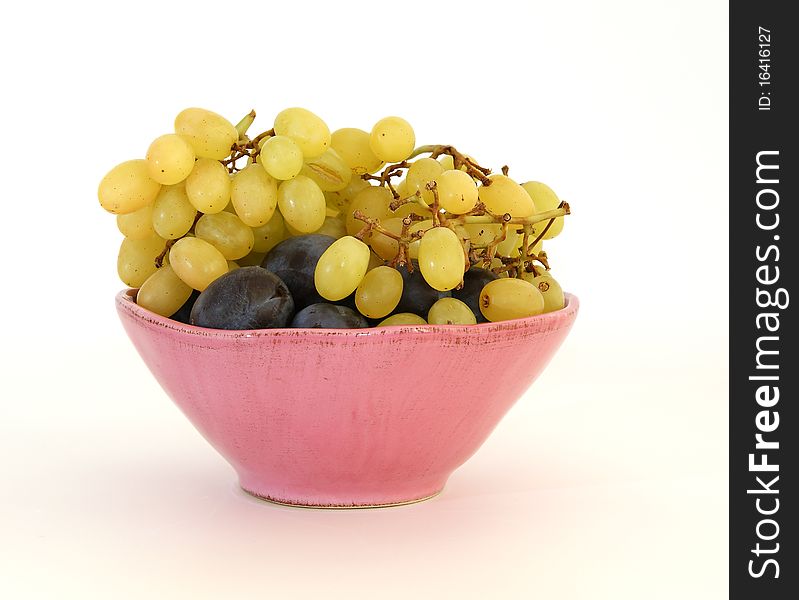 Still life of grapes and plums in a pink vase on a white background